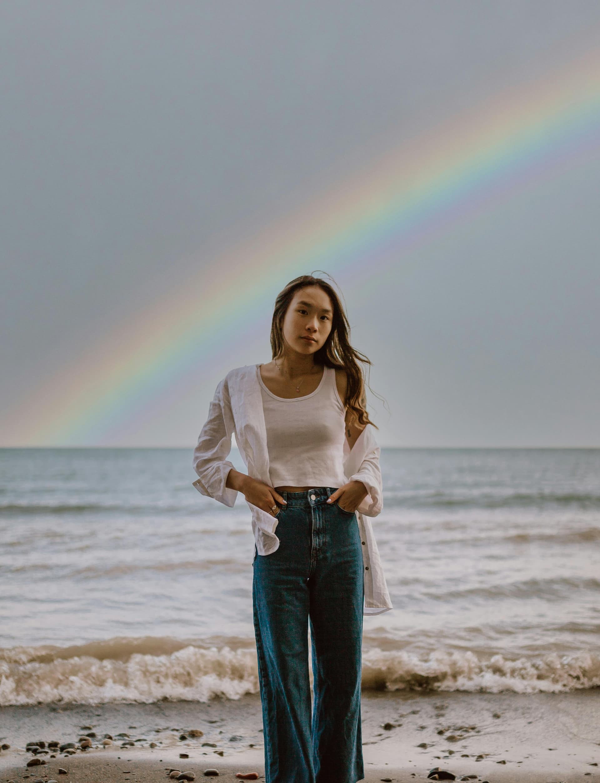 A woman standing on a beach with a rainbow in the background