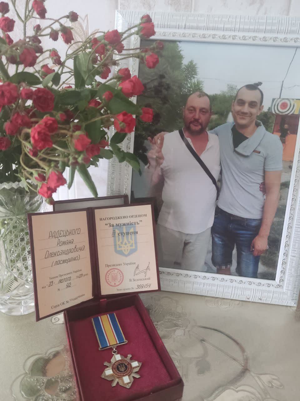 A couple of men standing next to a vase of flowers