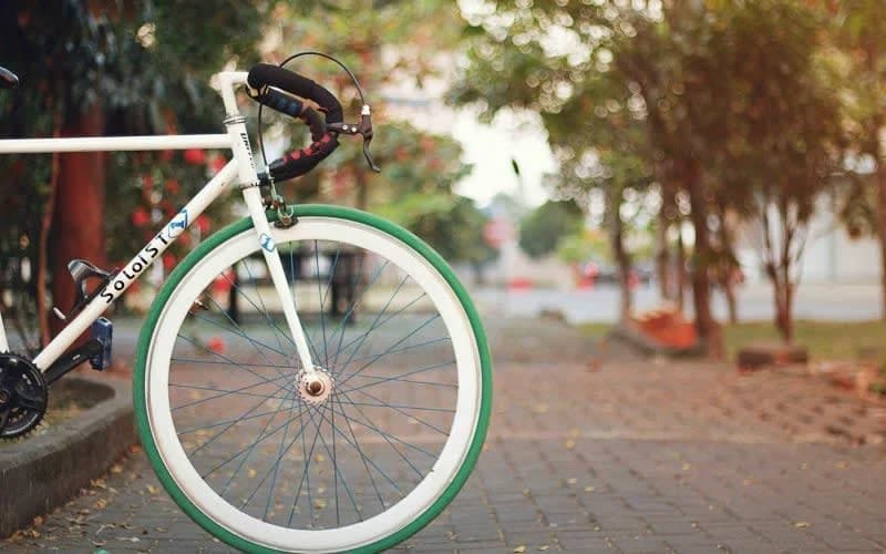 A white and green bike parked on a sidewalk