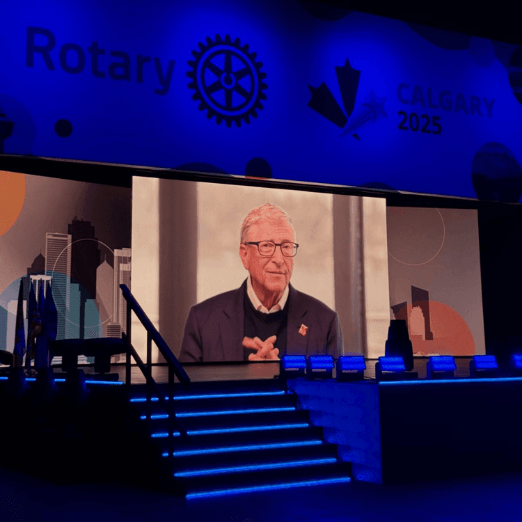 A man on a stage with a video screen in front of him