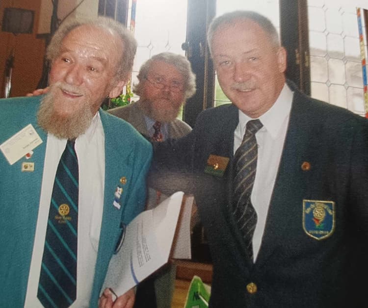 Two men standing next to each other in front of a window