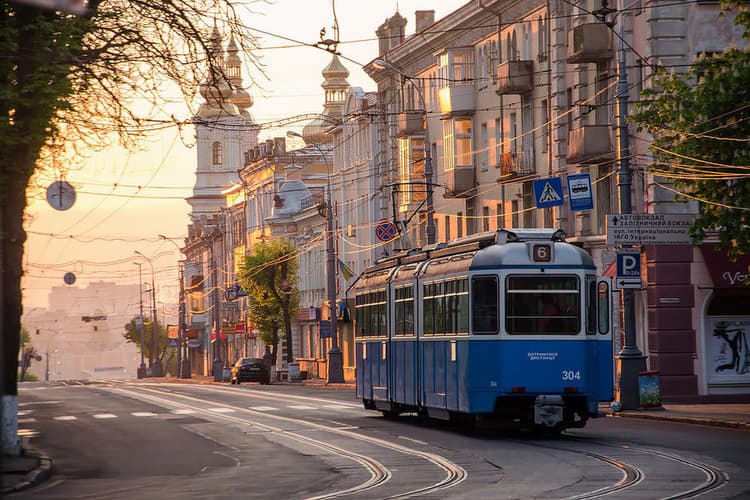 A blue and white train traveling down a street next to tall buildings
